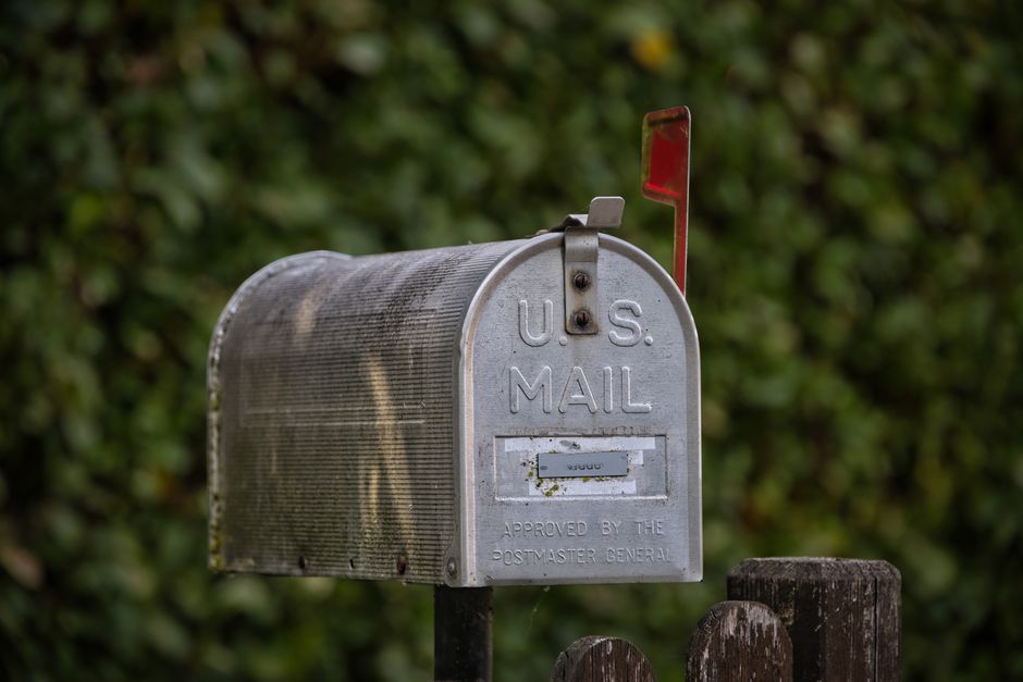 A traditional U.S. mailbox with red flag against a lush green blurred background.