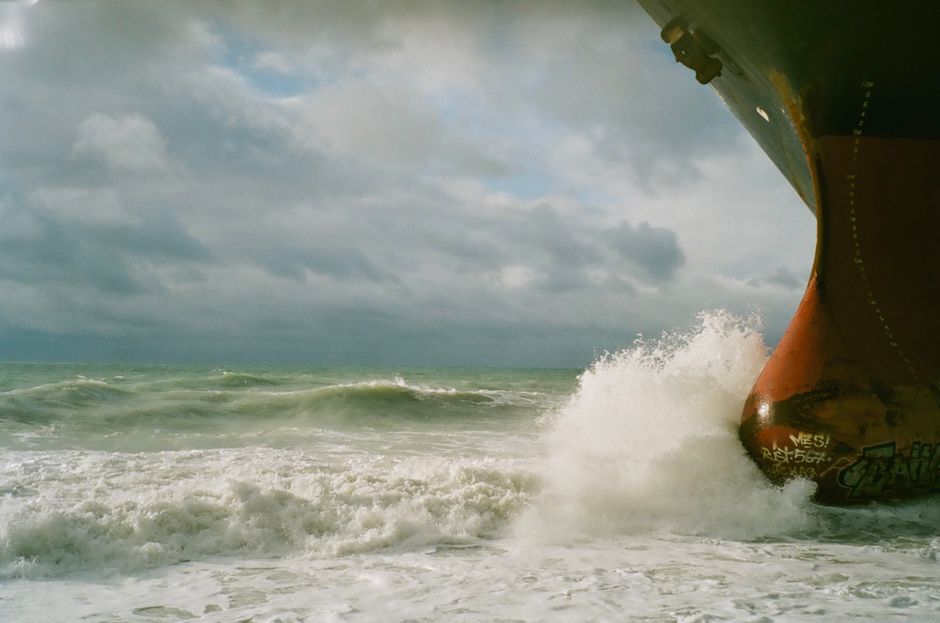 A powerful image of a ship's bow breaking through ocean waves under a cloudy sky, embodying sea travel adventure.